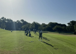Golfers walking on a sunny golf course with clubs.